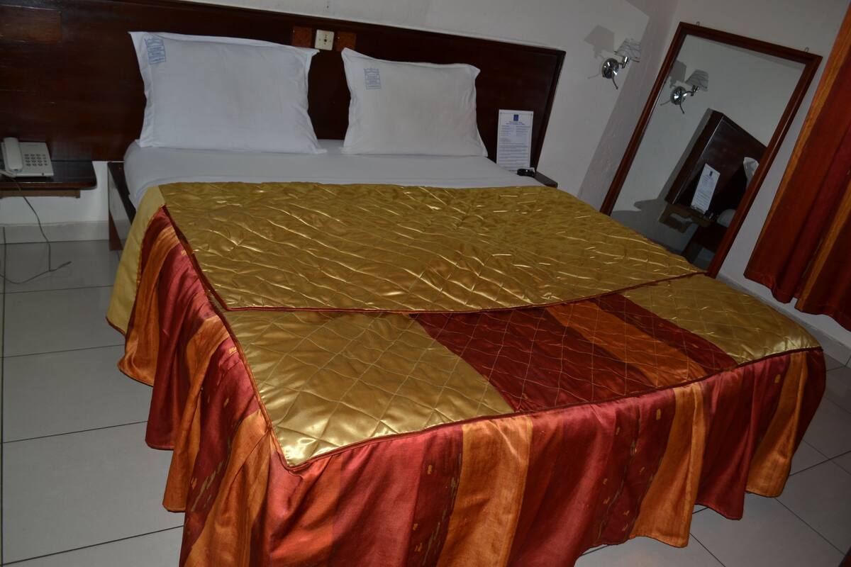 A hotel room with a bed, a nightstand, a telephone, and a mirror.