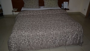 A bed with a patterned bedspread, a wooden headboard, and a bedside table with a phone. - Hôtel Lumière D'Akwa (Douala)
