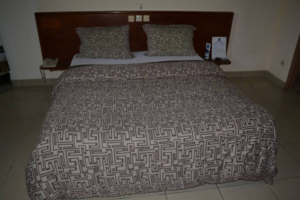 A bed with a patterned bedspread, a wooden headboard, and a bedside table with a phone.