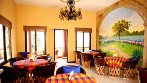 A dining area with multiple tables and chairs, a chandelier, and a mural of a landscape. - Las 7 Maravillas - Adults Only (Mazatlán)