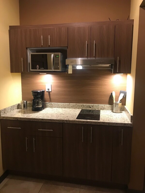 Una cocina con armarios de madera oscura, microondas de acero inoxidable, cafetera y horno empotrado.