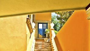 A staircase with white balustrades leading to a door with a blue frame, surrounded by yellow walls and potted plants. - Las 7 Maravillas - Adults Only (Mazatlán)