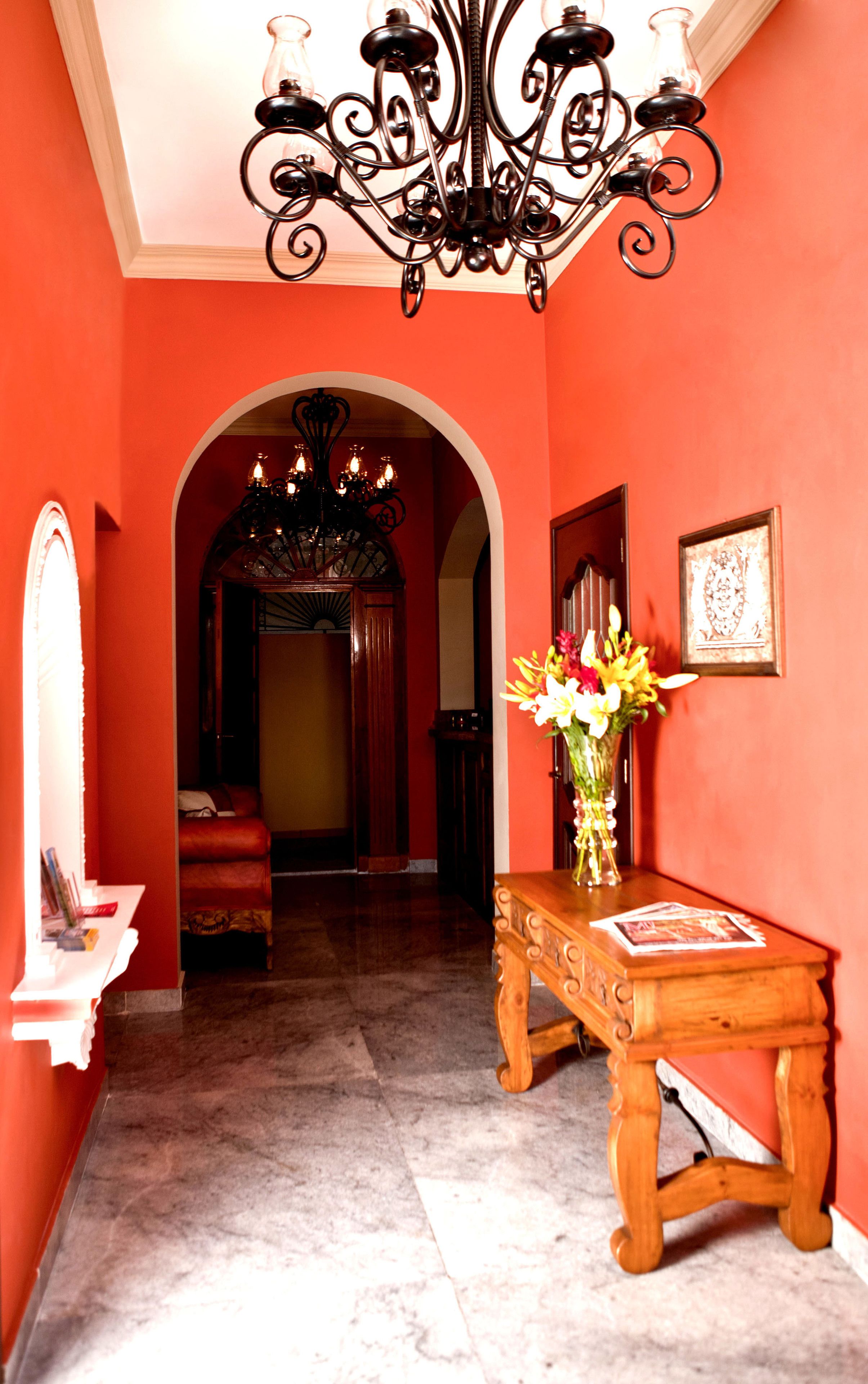 A hallway with a chandelier, a wooden console table with a vase of flowers, and a framed picture on the wall.
