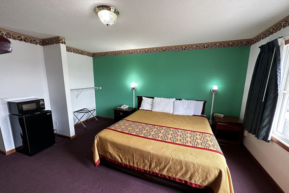Una habitación de hotel con una cama, un escritorio con teléfono, un microondas y un perchero.