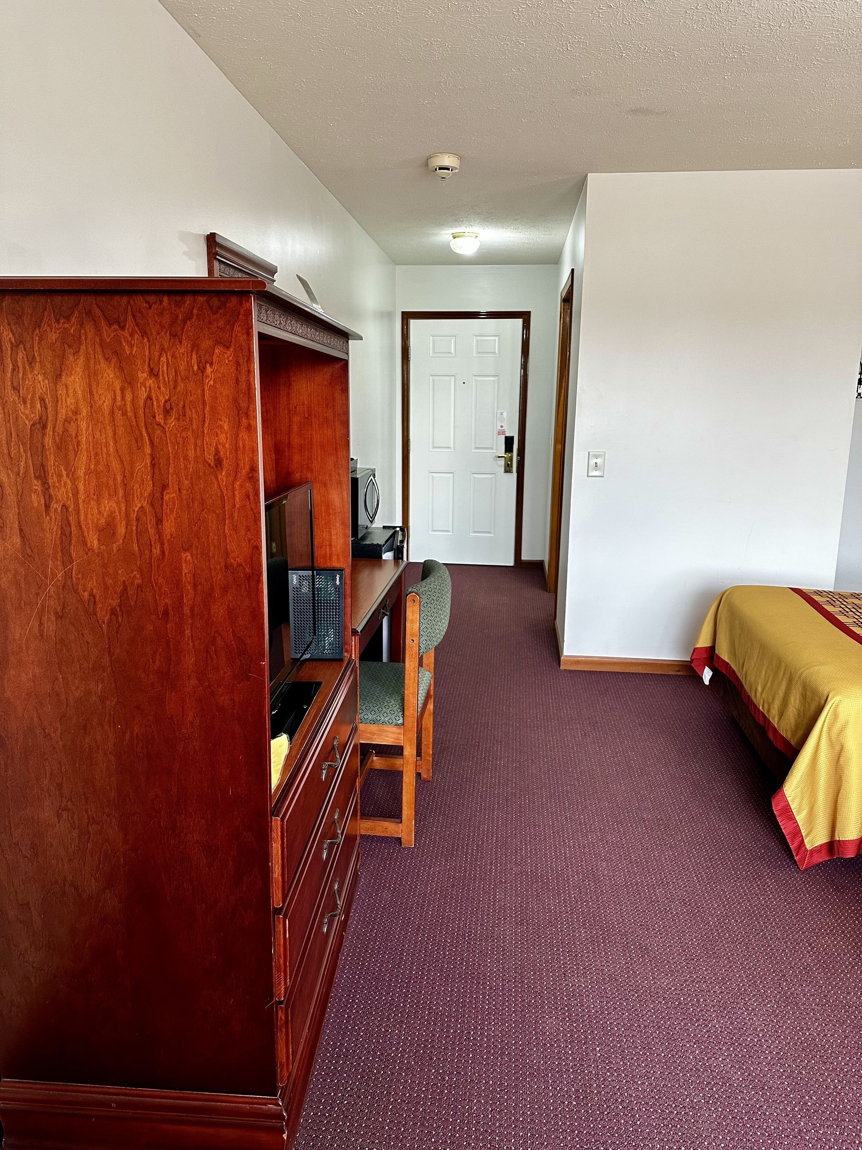 A room with a wooden dresser, a desk with a chair, a bed with a yellow bedspread, and a white door.