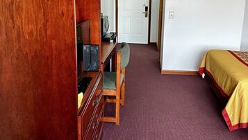 Una habitación con un aparador de madera, un escritorio con silla, una cama con colcha amarilla y una puerta blanca.