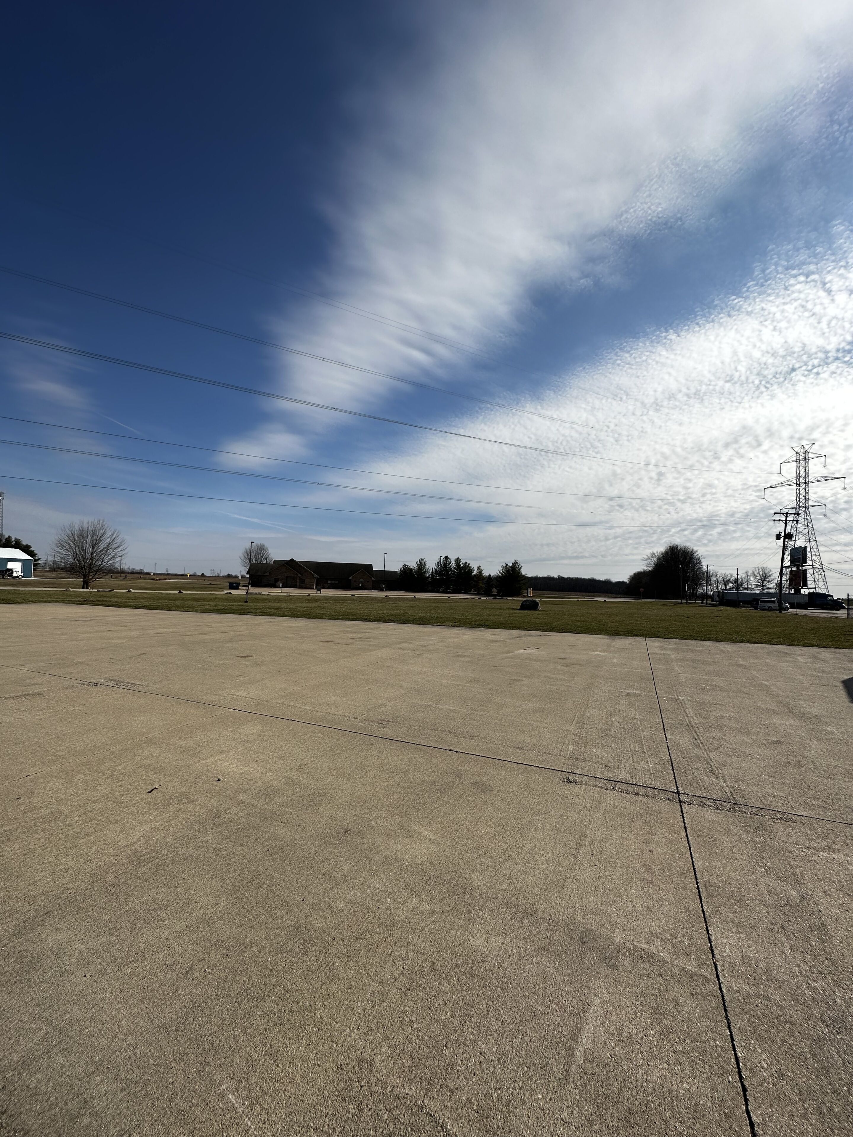 Une vaste zone ouverte en béton, avec un ciel dégagé et des lignes électriques.