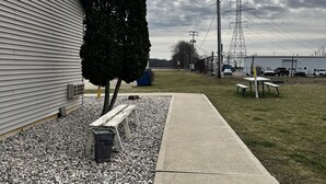 A building with a sloped roof, a gravel pathway, a bench, and a picnic table. - Attica Inn (Attica)