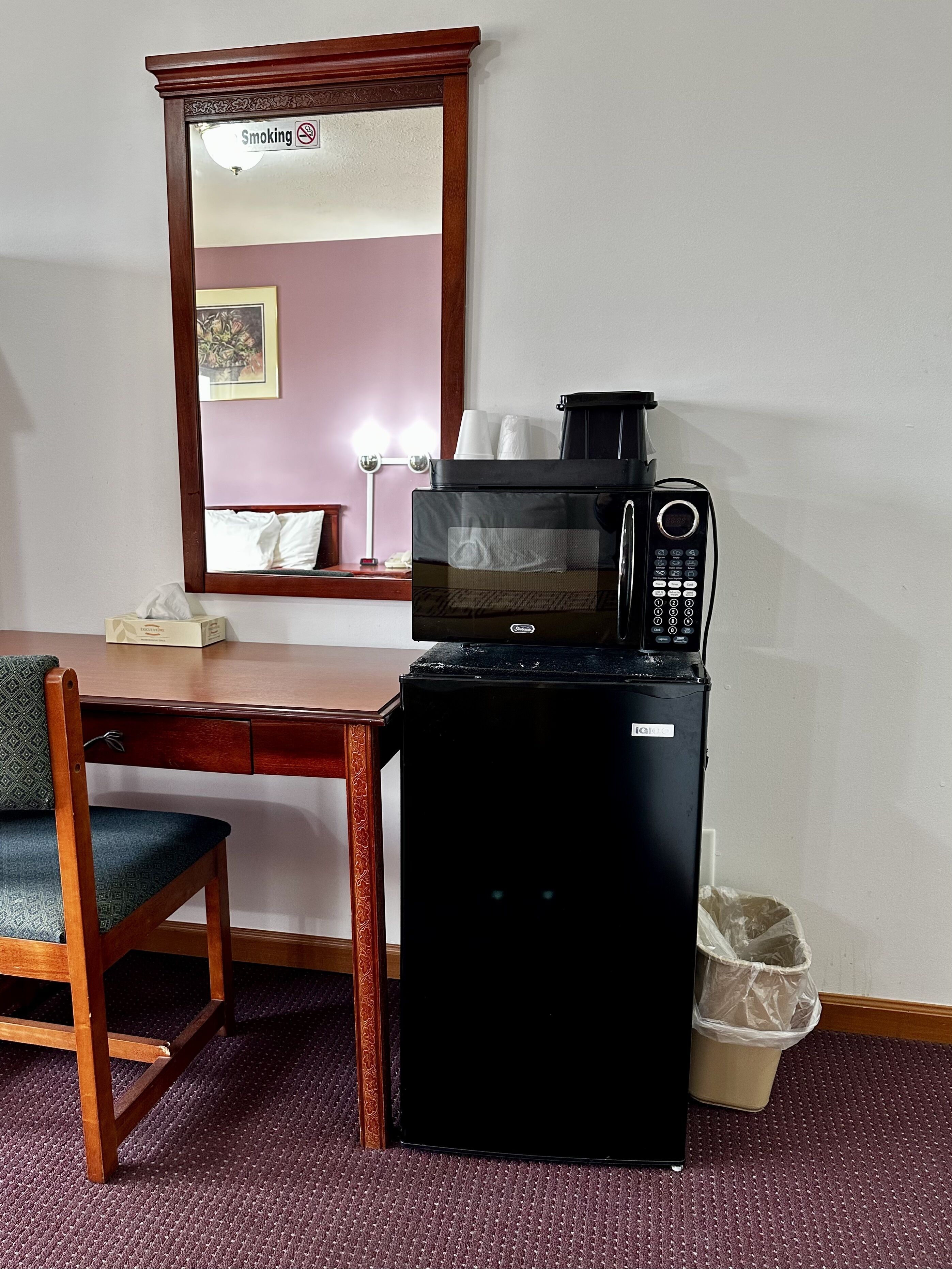 A compact kitchenette with a microwave, a small refrigerator, and a trash bin.