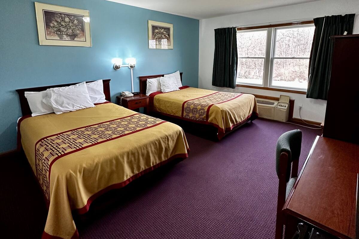 Habitación de hotel con dos camas, un escritorio y una ventana con cortinas.