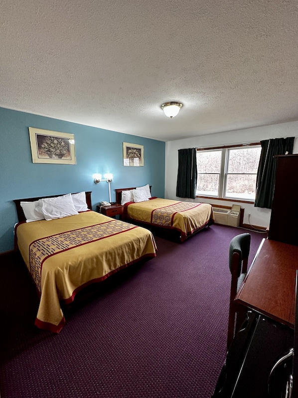 A hotel room with two beds, a desk, and a window with curtains.