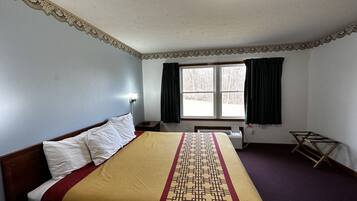 Una habitación de hotel con una cama, una ventana con cortinas, una mesita de noche y una lámpara fijada a la pared.