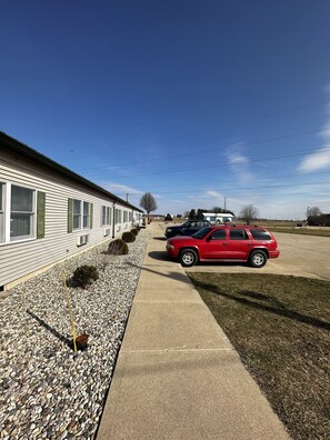 A mobile home with a red car parked in front, a clear sky, and a gravel driveway.
