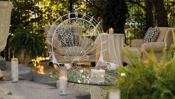 A glass-top table with a white metal fan, a beige sofa, and a candle in a garden setting.
