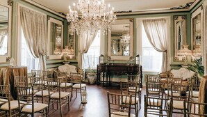 A room with a large chandelier, multiple chairs, a piano, and mirrors on the walls. - Maxwell Mansion (Lake Geneva)