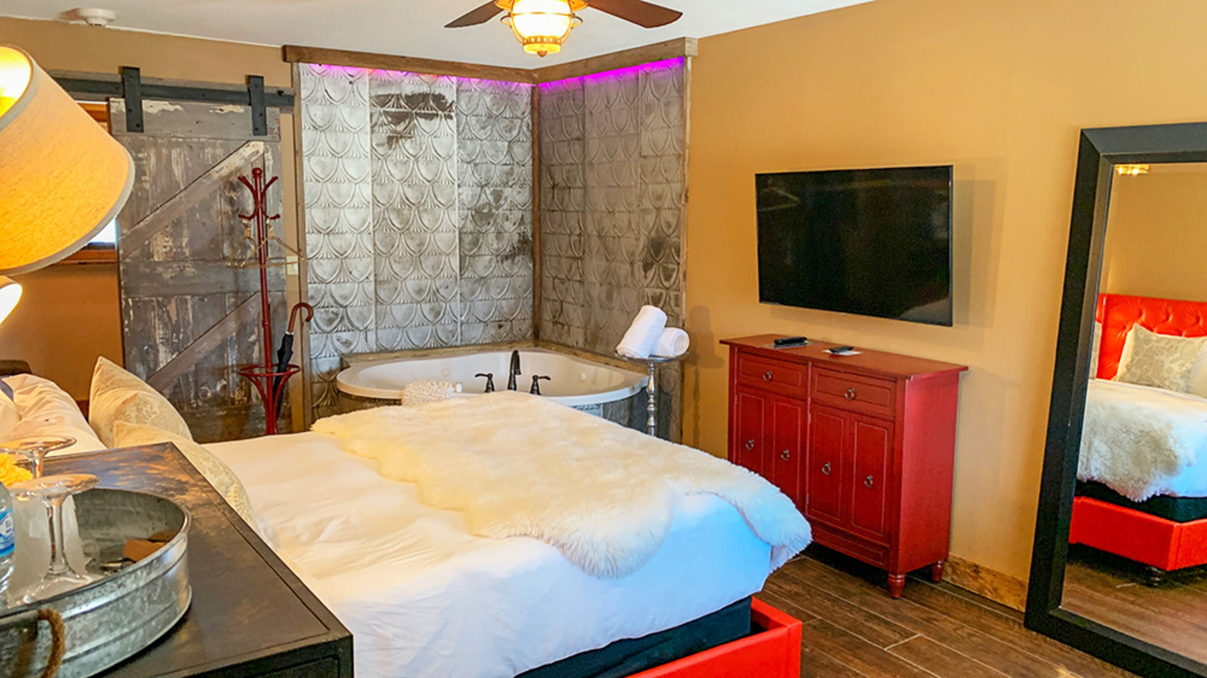 Quarto de hotel com uma cama grande, penteadeira vermelha, televisão, banheira e espelho.