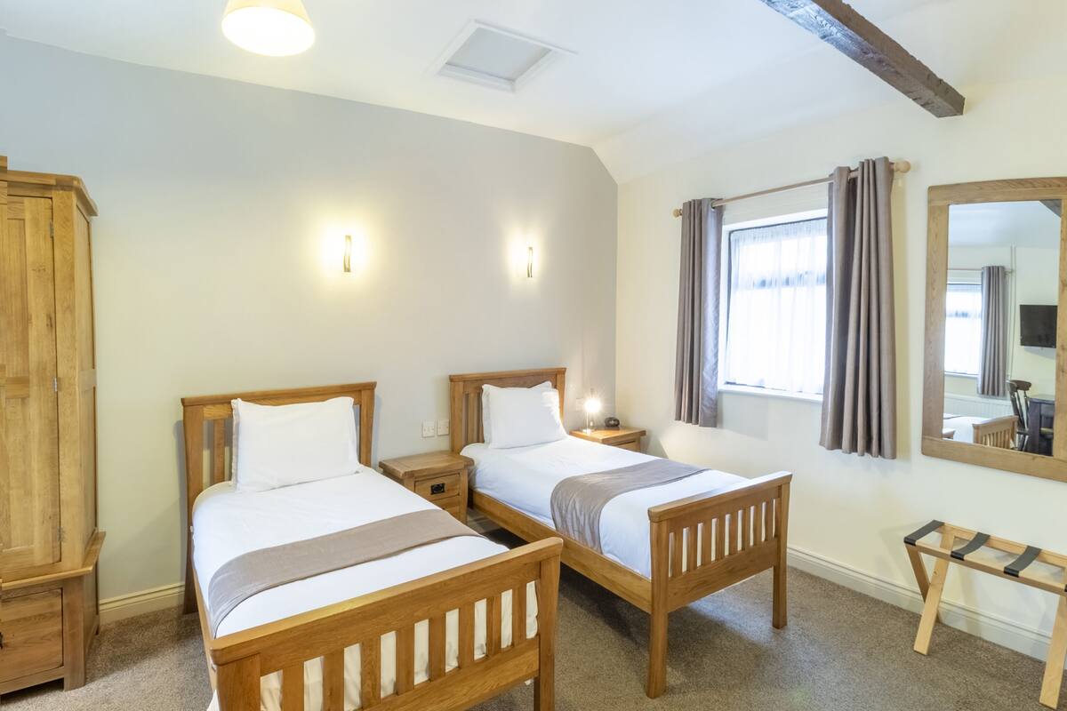 A room with two wooden beds, a wooden wardrobe, a small wooden table, and a mirror on the wall.