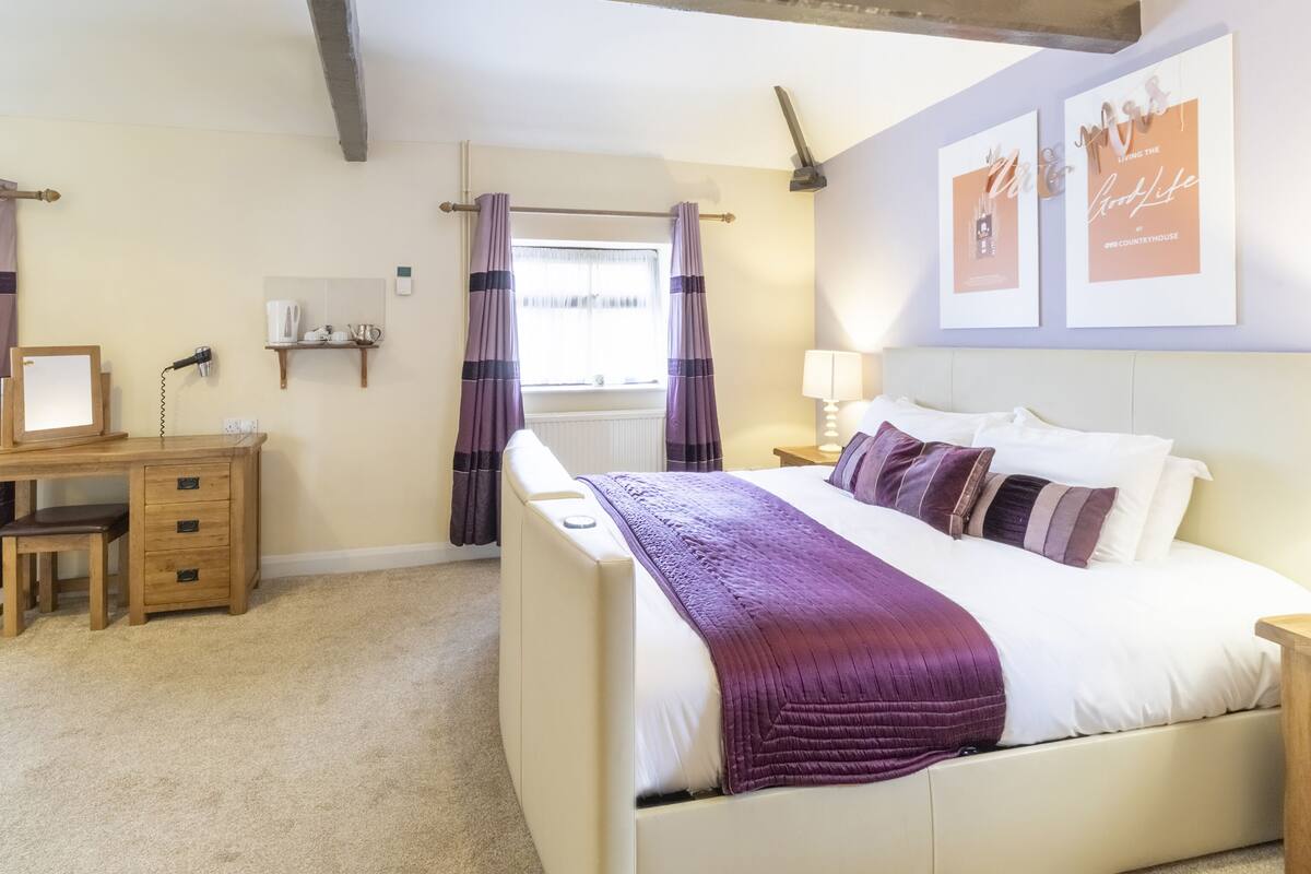 A bedroom with a bed, bedside table, lamp, and a desk with a chair.