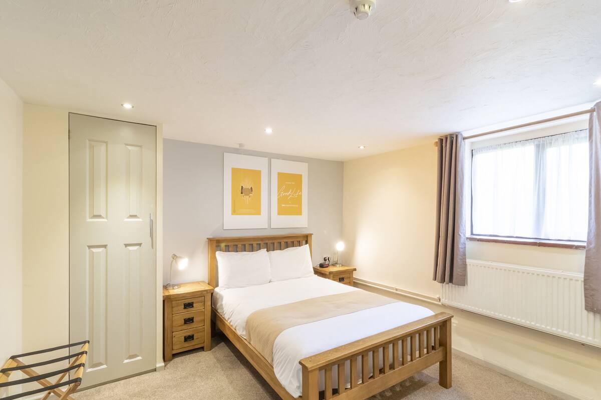 A bedroom with a wooden bed, a nightstand, a lamp, a radiator, and a window with curtains.