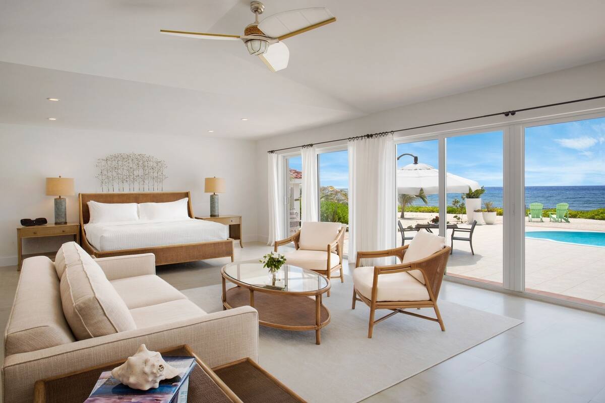 A spacious bedroom with a large bed, a sitting area with a coffee table, and a view of the ocean through large windows.