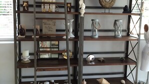 Una estantería metálica rústica con 'LESOLTPOR' exhibido en el estante superior, que sostiene varios objetos decorativos como velas, una campana y un cartel.