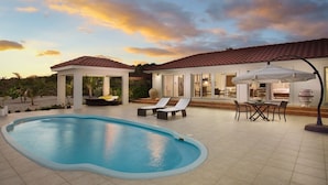 Una piscina con sillones de descanso, un porche cubierto y una zona de comedor con mobiliario exterior.