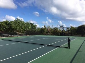 A tennis court with a net, surrounded by trees and a clear sky. - Le Soleil d'Or (West End)