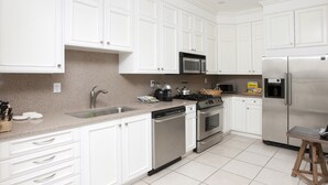 Una cocina moderna con armarios blancos, electrodomésticos de acero inoxidable y suelo de baldosas.