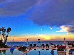 A poolside area with lounge chairs and umbrellas, overlooking the ocean at sunset. - My Resort HuaHin E503 (Hua Hin)