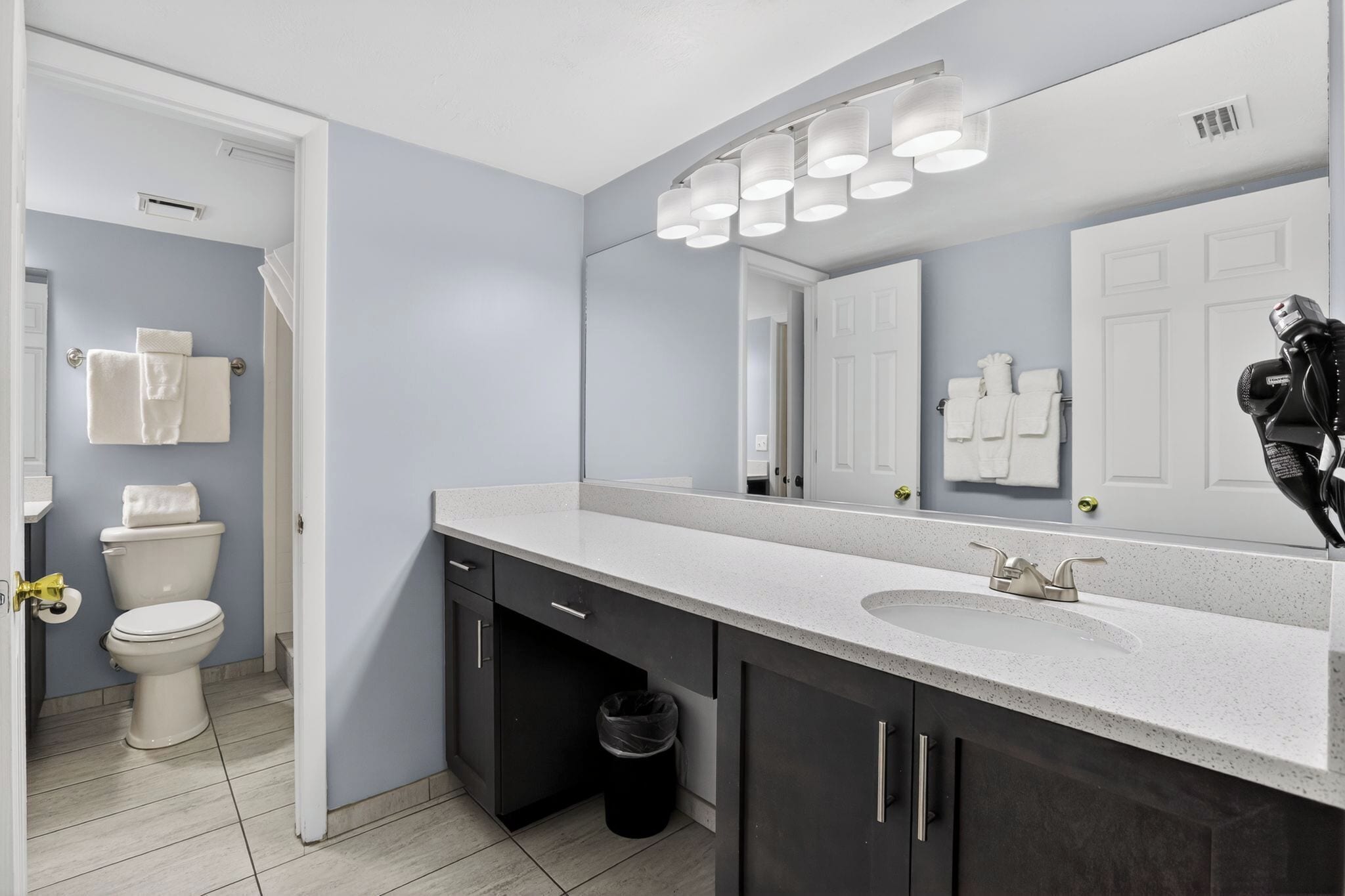 A modern bathroom with a white sink, dark cabinets, a large mirror, and a toilet.