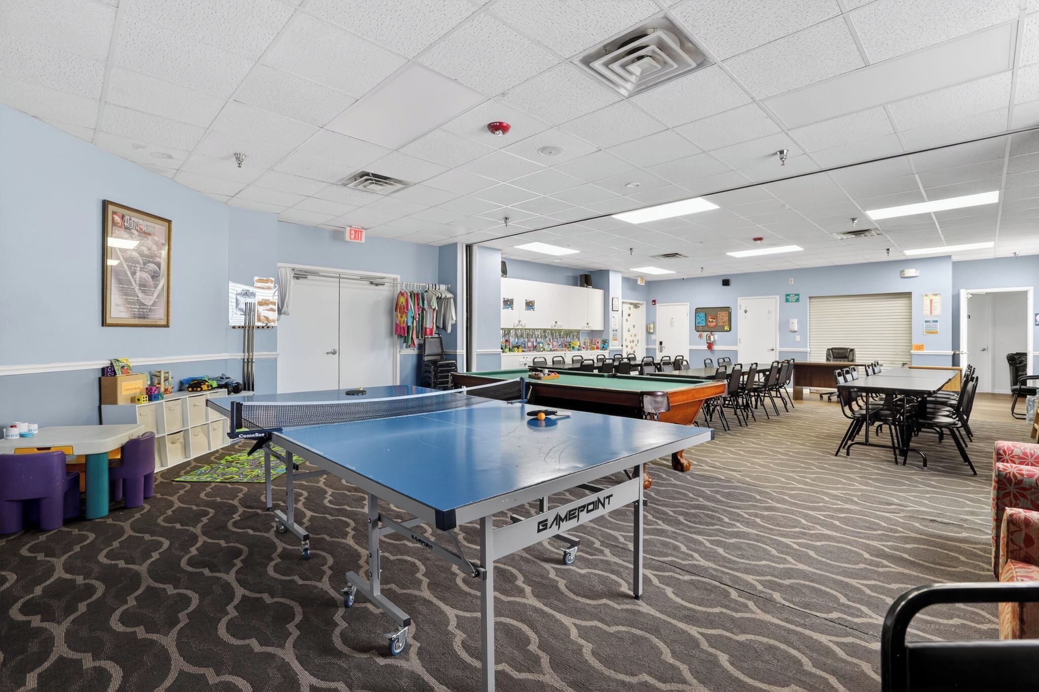 A room with a ping pong table, pool table, chairs, and a carpeted floor.