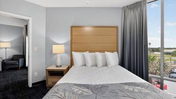 A hotel room with a bed, a nightstand, a lamp, a chair, and a view of the parking lot.