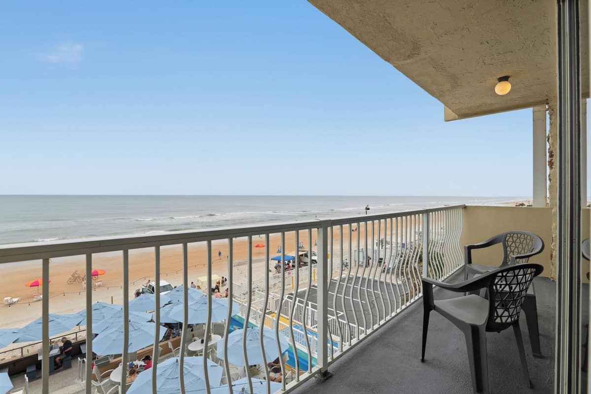 Un balcón con vistas a la playa, mobiliario exterior y sombrillas.