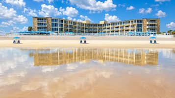Un hotel frente a la playa con un edificio curvo, varios balcones y asientos junto a la playa.