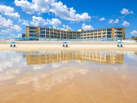 Un hotel fronte spiaggia con un edificio curvo, numerosi balconi e posti a sedere direttamente sulla spiaggia.