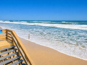 Una escalera de madera que lleva a una playa con agua azul cristalina y un cartel que indica una habitación preparada para el invierno.