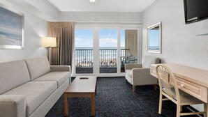 Une chambre d’hôtel équipée d’un canapé, d’un bureau, d’une chaise, d’une lampe, d’un ventilateur de plafond, d’une télévision et d’un balcon avec vue sur la plage.