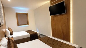 Habitación de hotel con dos camas, un televisor de pantalla plana montado en un panel de madera y un ventanal con vistas.