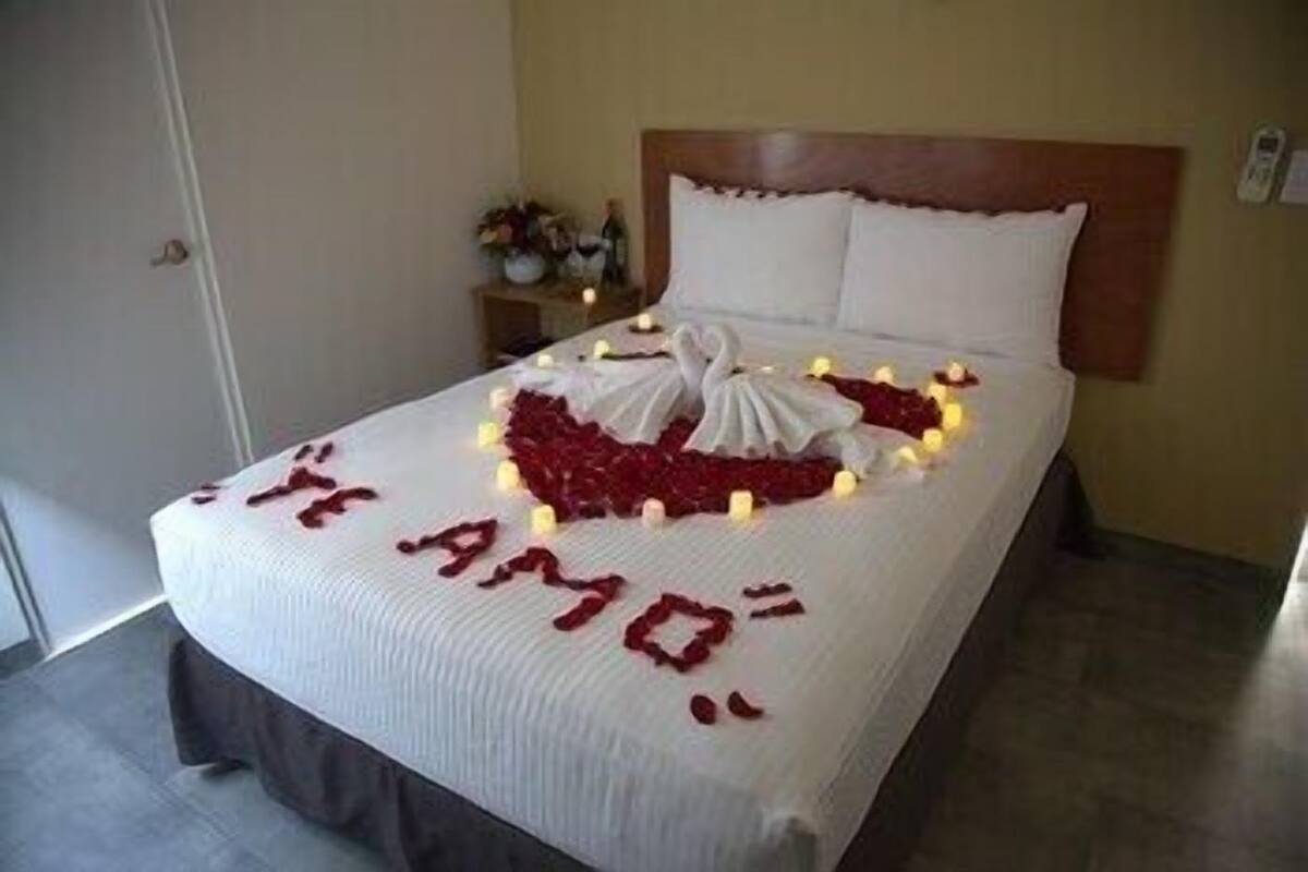A bed with a heart-shaped arrangement of rose petals and candles, and the words 'I LOVE YOU' spelled out on the bedspread.