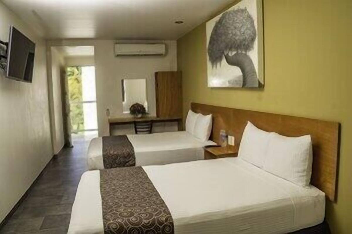 A hotel room with two beds, a desk, a chair, a mirror, and a painting on the wall.