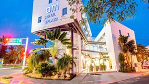 Un hotel moderno con un llamativo letrero que dice 'Om Hotel & Plaza', que presenta una estructura de varios pisos con balcón y pasillo cubierto.