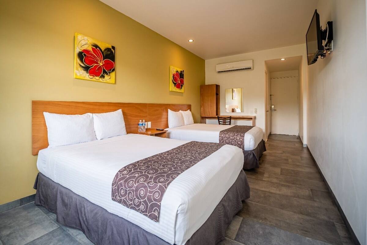 A hotel room with two beds, a wooden headboard, a desk, a chair, and a mirror.