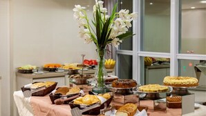 A buffet table with various baked goods and a vase of white flowers. - Tri Hotel Executive Brusque (Brusque)