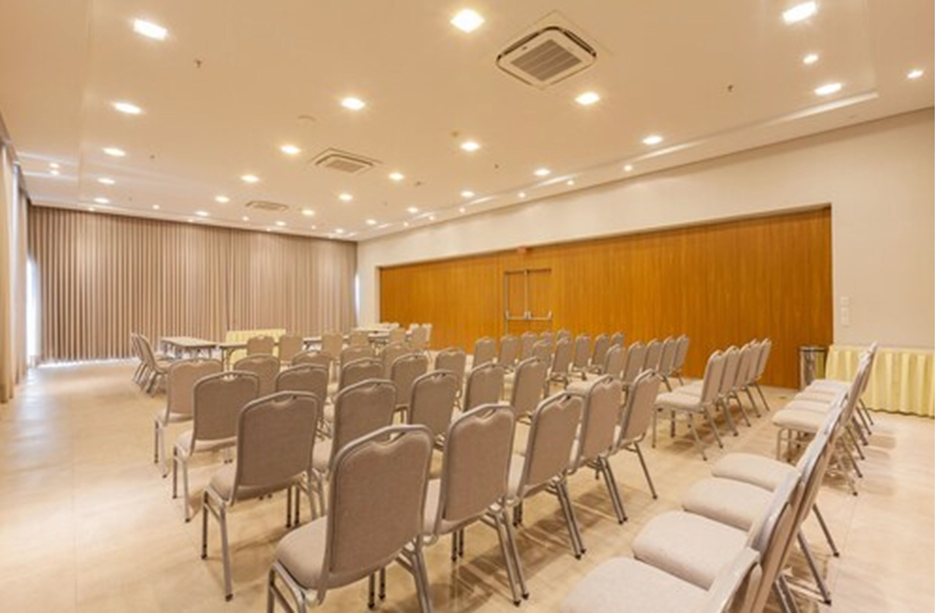 Uma sala de conferências com fileiras de cadeiras, painel de parede de madeira e luminárias no teto.