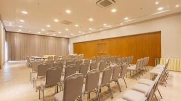 Uma sala de conferências com fileiras de cadeiras, painel de parede de madeira e luminárias no teto.