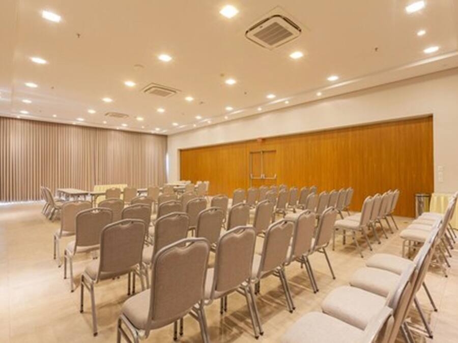 A conference room with rows of chairs, a wooden panel wall, and ceiling lights.