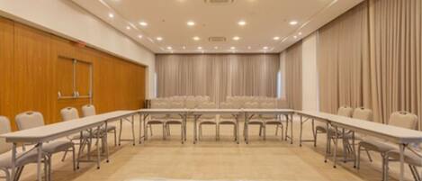 Un salón de conferencias con una mesa larga y sillas, paneles de madera en una pared y cortinas en otra.