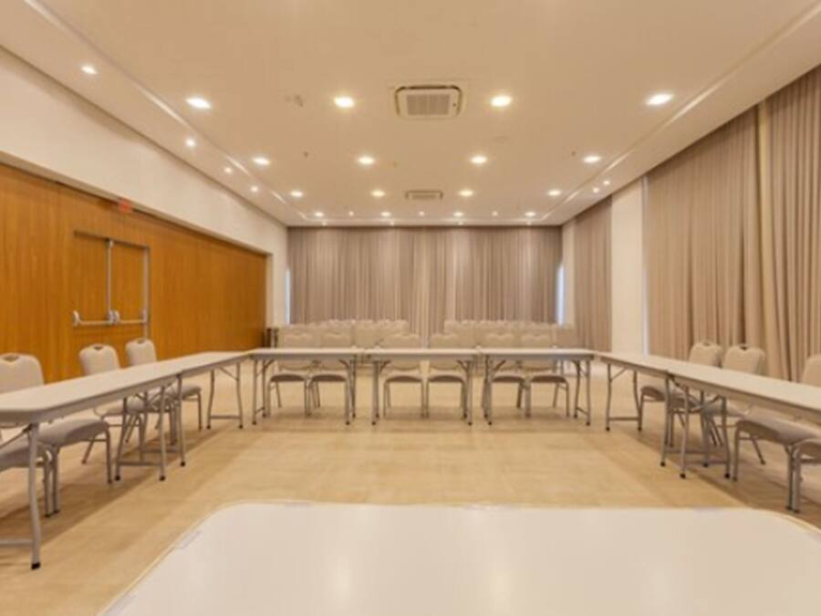 Un salón de conferencias con una mesa larga y sillas, paneles de madera en una pared y cortinas en otra.