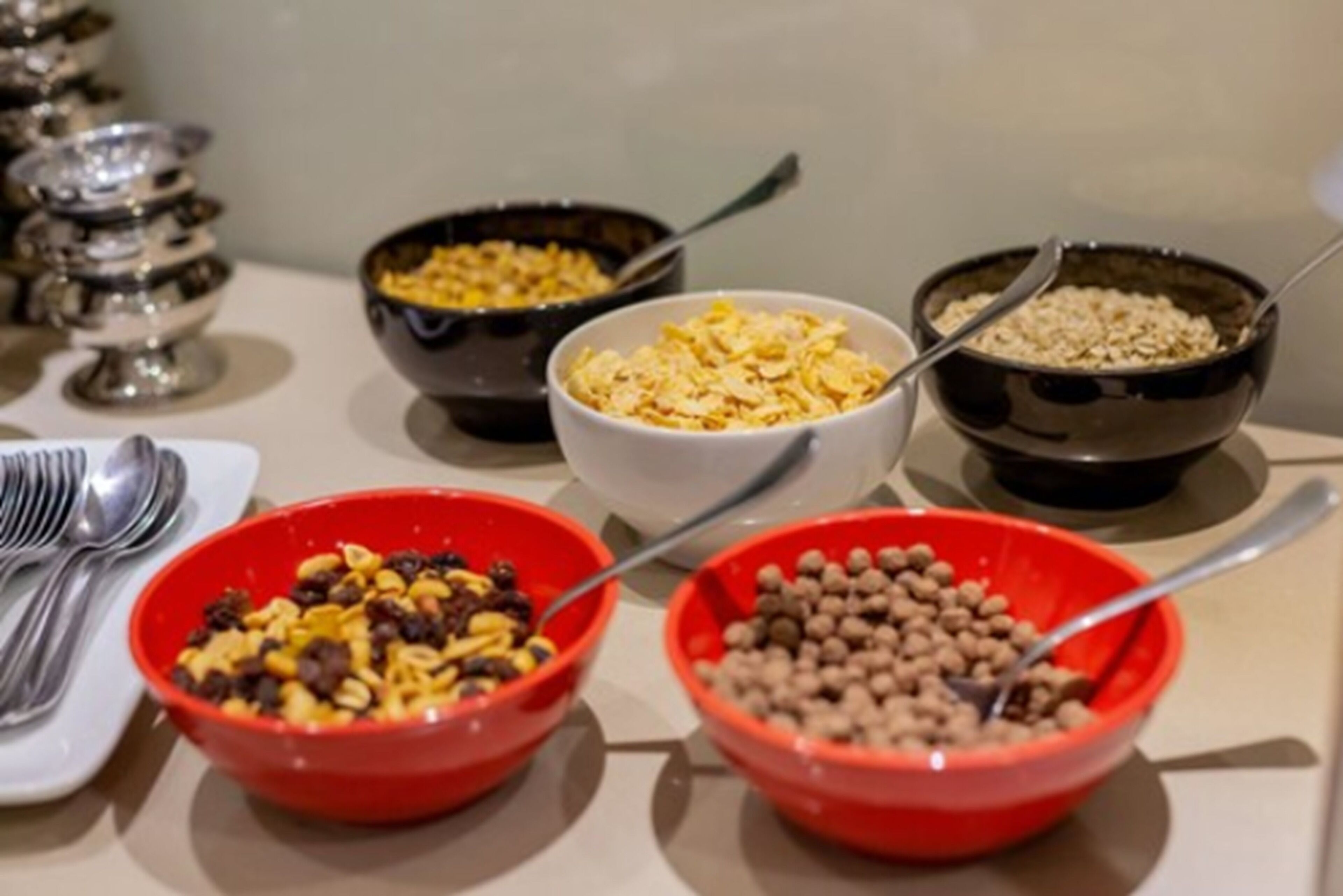 A buffet table with various food items in bowls, including cereal, nuts, and dried fruits.
