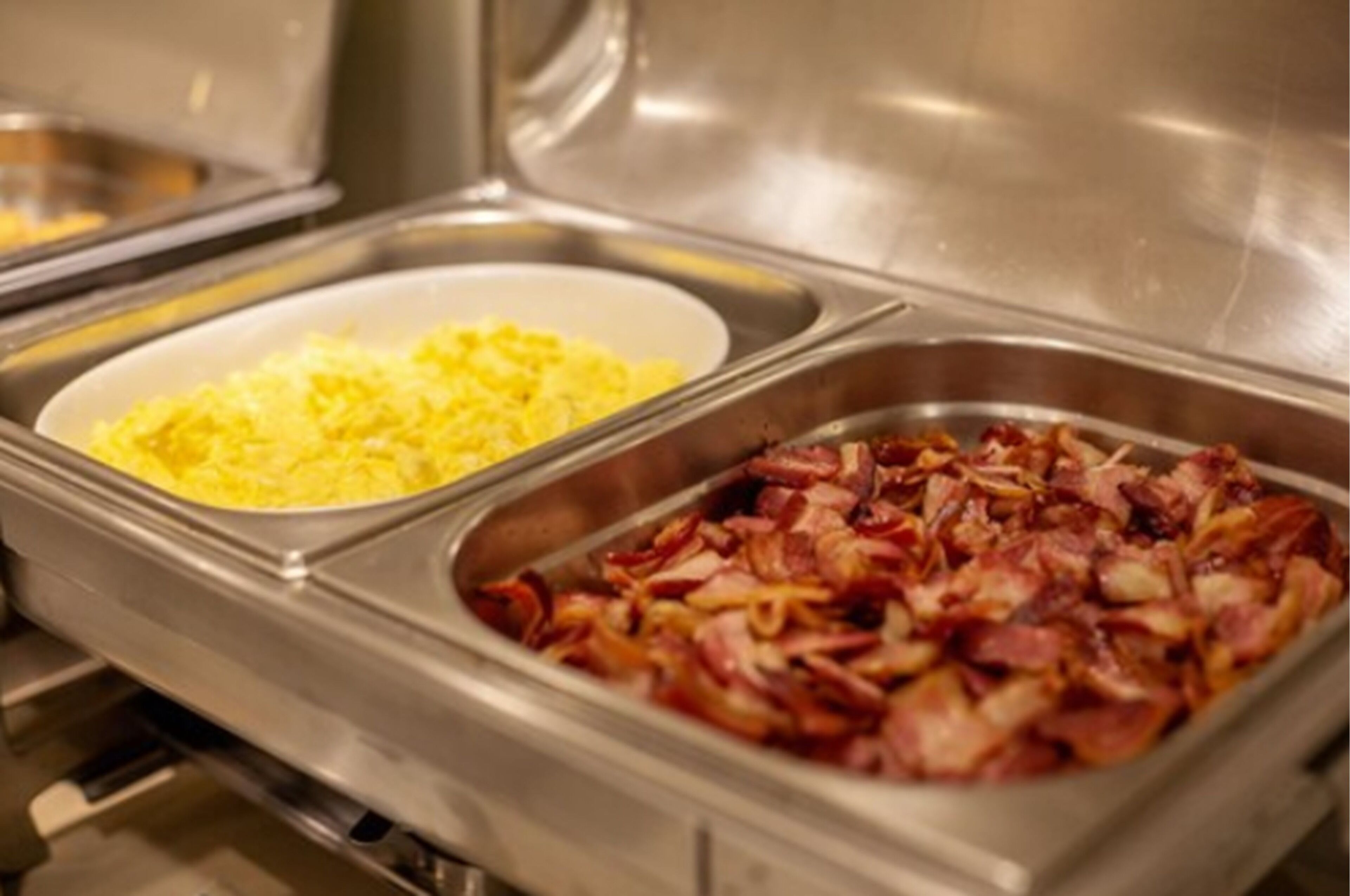 A buffet with two dishes: one with scrambled eggs and another with bacon.